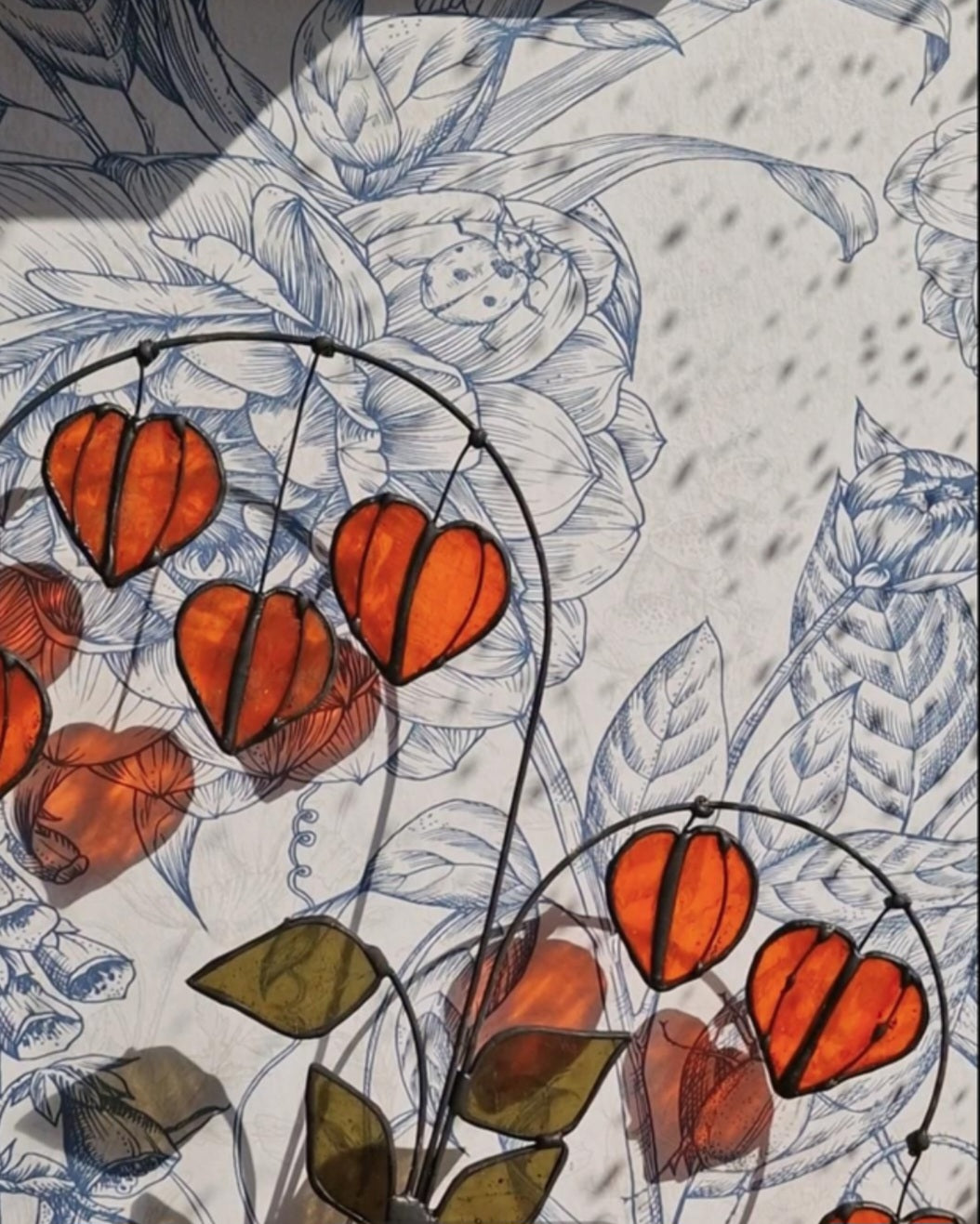 Chinese Lantern Plant Stem: “Orange stained glass Chinese lantern stems with green leaves displayed in a white vase.”