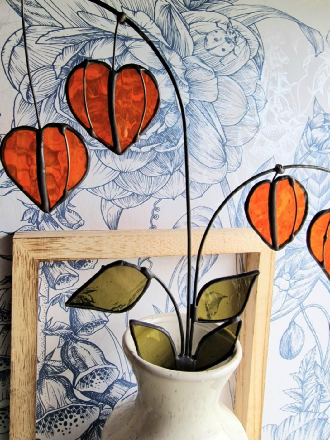 Chinese Lantern Plant Stem: “Orange stained glass Chinese lantern stems with green leaves displayed in a white vase.”